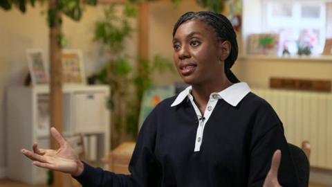Kemi Badenoch speaking in a black shirt with a white buttoned collar