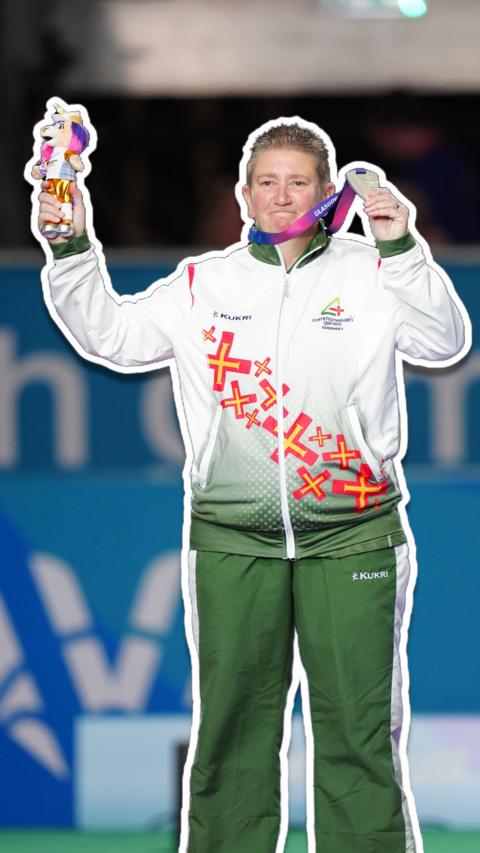 A woman in a green and white tracksuit holding up a silver medal and a unicorn soft toy