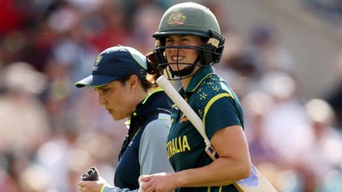 Ellyse Perry grimaces as she walks off the field alongside the Australia physio