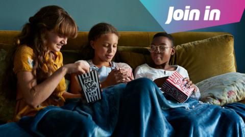three girls eating popcorn under a blankey