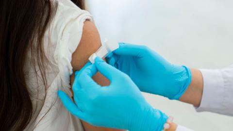 A person wearing blue latex gloves placing a plaster on a person's arm.