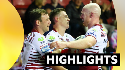 Three Wigan players stand facing each other in a hug after a try