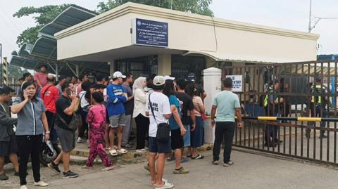 People crowd outside the gate of the Ateneo de Zamboanga junior high school where a shooting left two students dead