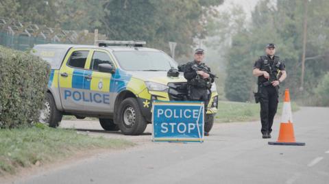 Police stand near a stop sign and a police vehicle near RAF Fairford