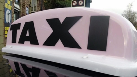 A close up image of a sign on the top of a car reading 'Taxi'