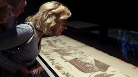 Blonde woman leaning over Bayeux Tapestry