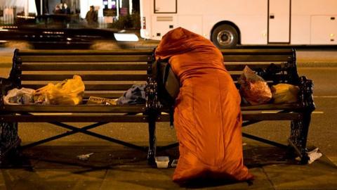 A photo of a homeless person in a sleeping bag on a bench 