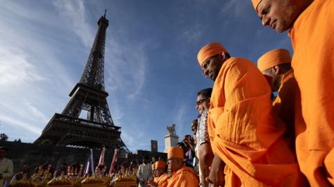 Hindu monks stand in front of the Eiffel Tower wearing traditional orange robes.