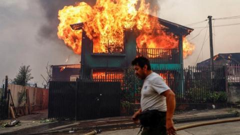 A man walks past a building on fire in the Biobio region of Chile