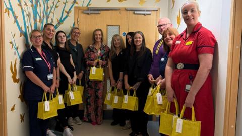 A group of nurses and charity members stood in a hospital corridor with yellow bags