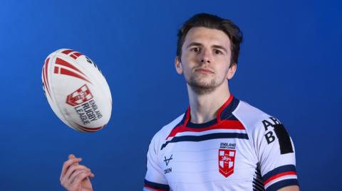Rob Hawkins, wearing an England shirt, throws a ball in the air
