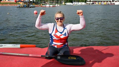Charlotte Henshaw celebrates with her arms raised having just got out of her kayak