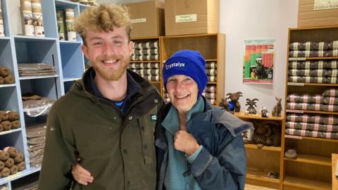 Jamie Robinson and Jenny Shepherd in the farm shop at Ballacosnahan Farm. Balls of wool are visible on the shelves behind them.