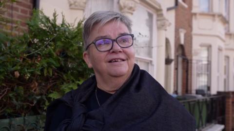 Woman with short grey hair with black glasses standing in a street