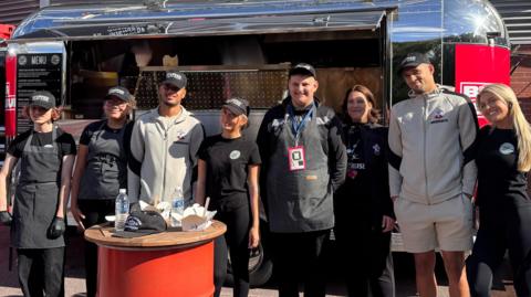 Employees and people in Southampton tracksuits stand in front of the Stuffed food truck outside St Mary's.