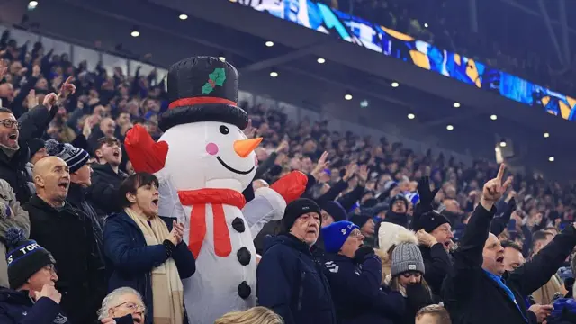 A fan dressed in a snowman costume looks on