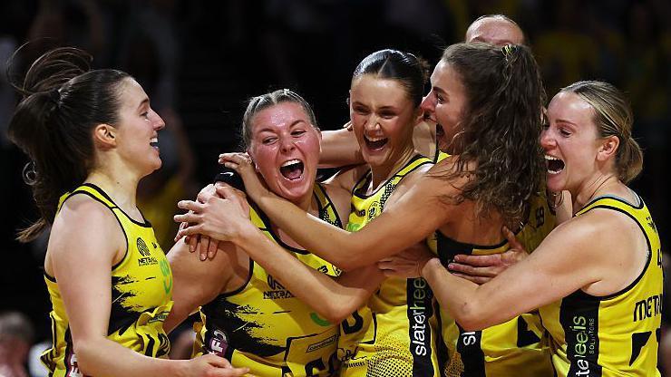 Eleanor Cardwell celebrates with joyful team-mates at the moment when AO Manchester Thunder, in largely yellow netball outfits, win a fifth Super League title