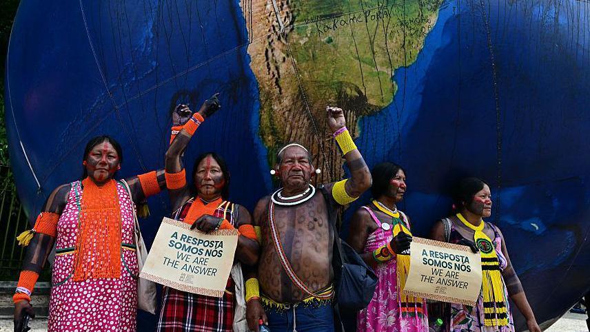 Indigenous people pose next to a giant inflatable globe during the "Indigenous People Global March" at the COP30 UN Climate Change Conference in Belem, Para state, Brazil, on November 17, 2025.