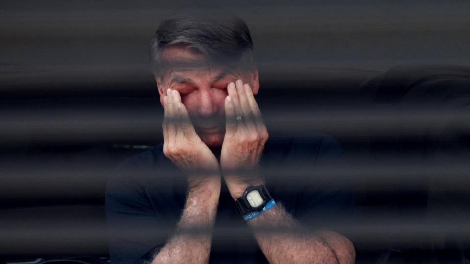 Jair Bolsonaro wipes his eyes with his hands in a photo captured through the blinds of a window of his home in Brasilia