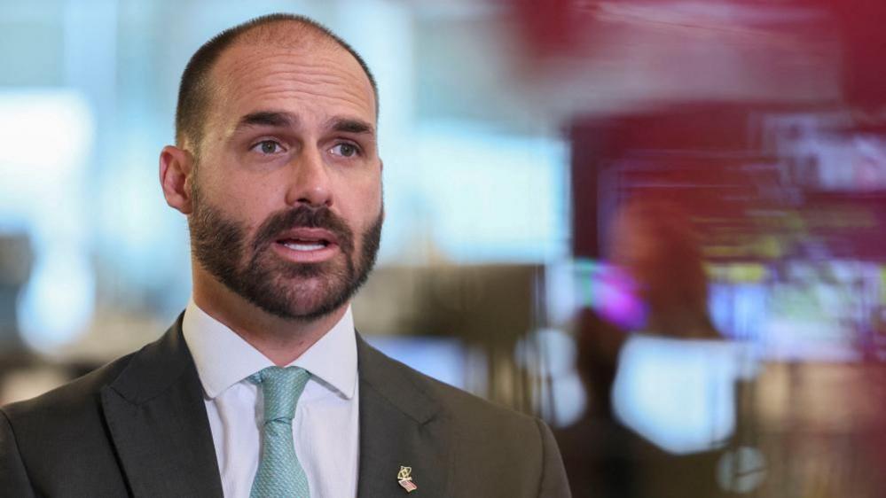 Brazilian lawmaker Eduardo Bolsonaro sits down, wearing a dark suit and blue tie