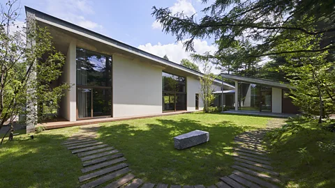 A modern asymmetrical house with roof sloping downwards to right with floor to ceiling windows and connected to a glass gust annexe to the right with landscaped Japanese garden in foreground (Credit: Masaya Yoshimura / A House in Japan/ gestalten 2026)