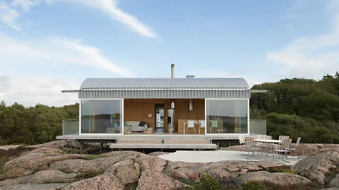 Åke E:son Lindman A timber and steel cabin with large sliding glass panels and an outdoor patio, situated on rocky terrain between two fjords in Sweden (Credit: Åke E:son Lindman)