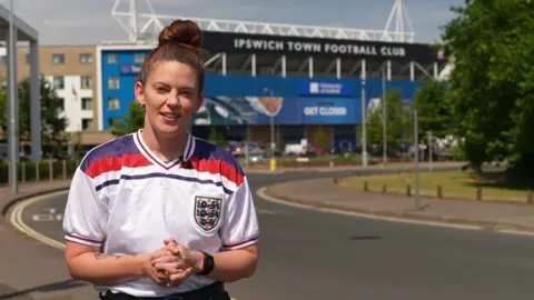Zoie O'Brien wearing an England shirt, outside Ipswich Town Football Club's stadium