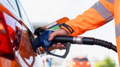 Close-up of a man refuelling orange car at gas fuel station. Male filling diesel at petrol station using a fuel nozzle