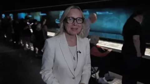 Correspondent Katie Razzall at exhibition, wearing white blazer and top
