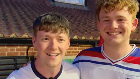 Two young male England fans smiling.