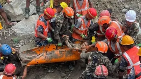 A group of rescuers holding a man on an orange stretcher.