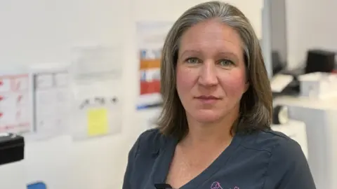 Vet Cate Titterton wearing dark blue scrubs standing in her surgery