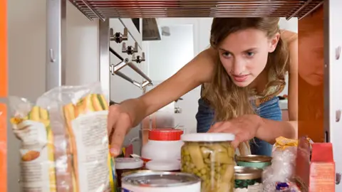Woman looks inside a storage area containing various food items