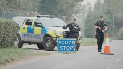 Police stand near a stop sign and a police vehicle near RAF Fairford