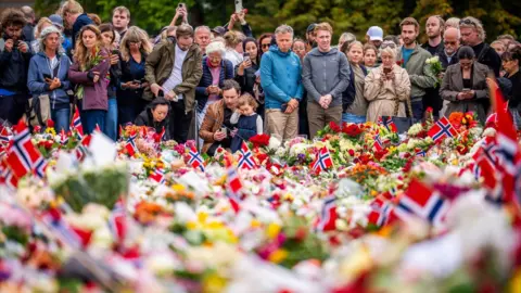 Mourners gather in Palace Square with candles, flowers and Norwegian flags