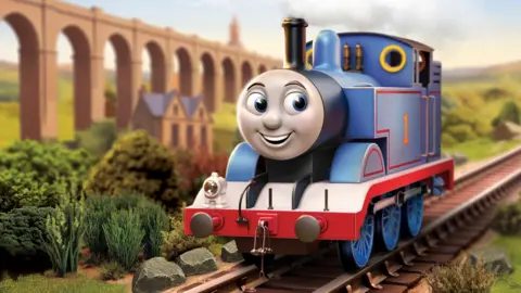 Still image from the 2026 Thomas the Tank Engine animation. Thomas is a blue engine with red livery. He is smiling. He is in the countryside and there is a tall viaduct with many arches on the left and a brick building in front of it.