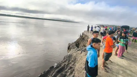A crowd of people stand on the bank of the Ucayali River