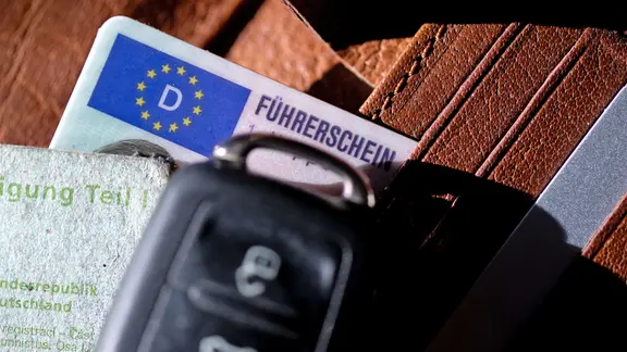 Ein Führerschein, ein Autoschlüssel und eine Zulassungsbescheinigung liegen auf einem Portemonnaie