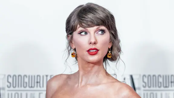 Eine Frau (Taylor Swift) mit brünettem, kurzem Haar blickt an der Kamera vorbei. 