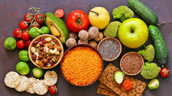 Linsen, Kohl, Knäckebrot, Walnüsse und veschiedene Gemüsesorten auf dunklem Untergrund. 