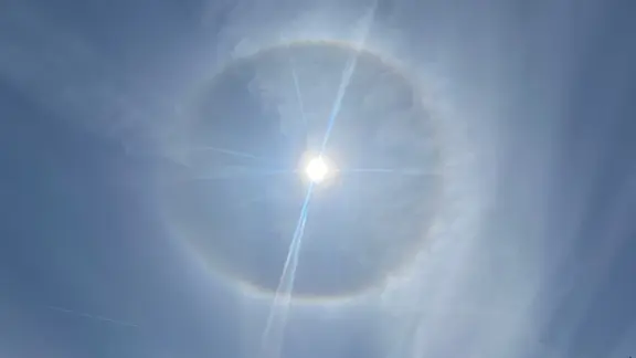 Ein Kreis aus Licht umspielt die hoch am Himmel stehende Sonne