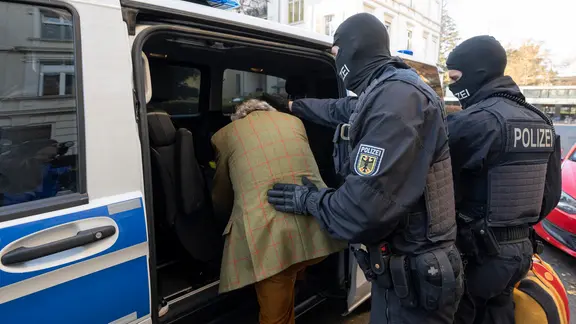 Bei einer Razzia gegen sogenannte Reichsbürger führen maskierte Polizisten den Verdächtigen Heinrich R. in Frankfurt zu einem Polizeifahrzeug.