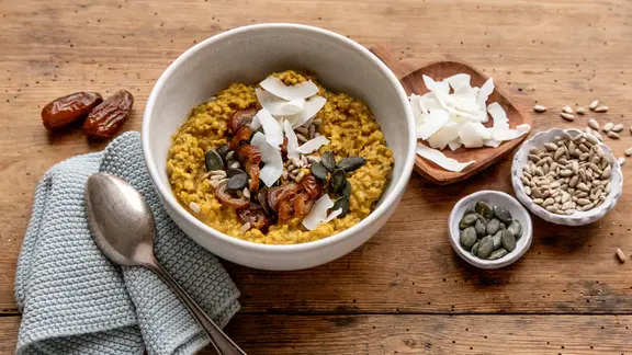Eine Schale mit Porridge, darauf Dattelstückchen und Kerne.