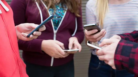 Eine Gruppe von Personen steht mit Smartphone in eienm Kreis