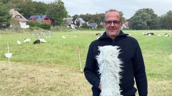 Stefan Kreibohm moderiert das Wetter vor einer Schafwiese. 