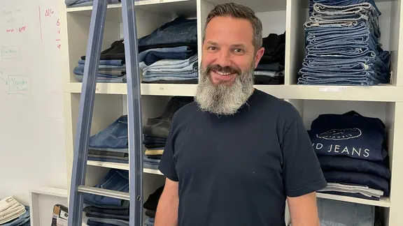 Dion Vijgeboom von der Jeansmarke MUD Jeans steht vor einem Regal voller Jeans.