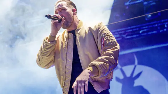 Der Musiker Danger Dan steht mit gelber Jacke auf einer Bühne in Berlin.