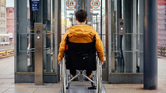Ein Mann mit einem Rollstuhl vor einem Aufzug.