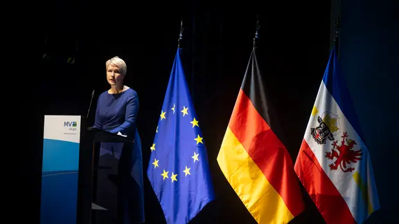 Ministerpräsidentin Manuela Schwesig steht neben drei großen Fahnen auf der Bühne im Schweriner Theaterzelt.