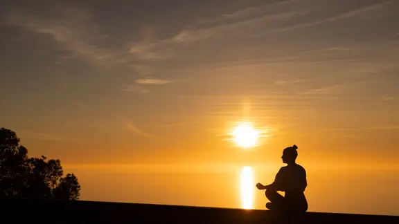 Eine Frau meditiert im Sonnenuntergang am Meer.